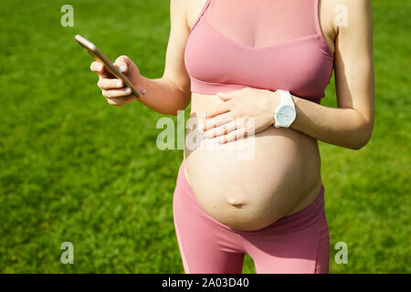 Close-up of young woman in pink top standing outdoors and using her mobile phone Stock Photo