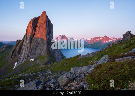 View from Mount Hesten on Iconic Mountain Segla in light of midnightsun in front of clear sky and mountain range in background, rocks and boulders in