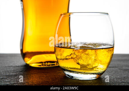 A simple and elegant whiskey (whisky) bottle and glass with ice on a dark stone base with a white background Stock Photo