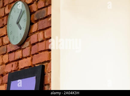 A clock with hands hangs on a rough brick wall. Another corner surface is finished and painted in white as a copy space. Contrast of two opposite cond Stock Photo