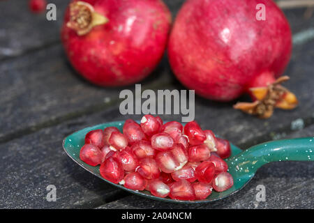 Still life of two pomegranates on wooden table and green metal spoon containing pomegranate seeds Stock Photo