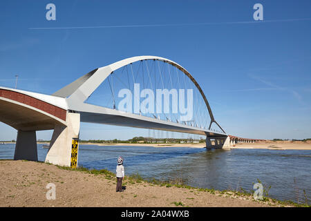 Young boy wearing helmet looking at the bridge named De Oversteek which spans the river Waal at Nijmegen Stock Photo