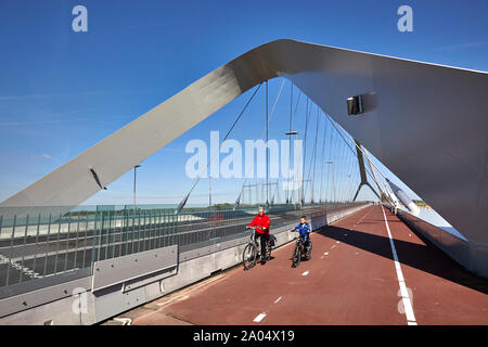 A female and young boy cycling on the bridge deck of a bowstring bridge named De Oversteek which spans the river Waal at Nijmegen Stock Photo