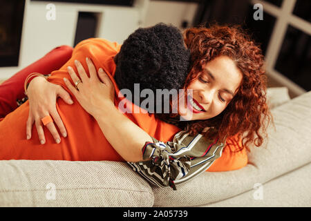 My love. Kind dark-skinned man embracing his wife while having rest in new apartment Stock Photo