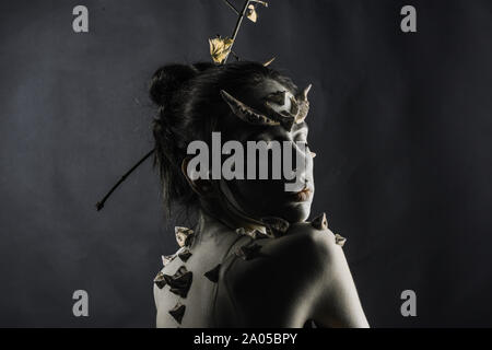 Nymph or forest spirit appearing from darkness, fairy tale concept. Skinny girl with thorns on back and horns on head isolated on black background Stock Photo