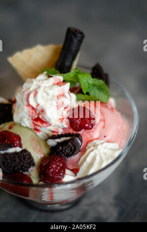 raspberry and pistachio ice cream sundae dessert in glass bowl with chocolate cookies and berries