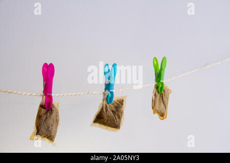 Three used teabags hang to dry on a washing line with colourful pegs, against a neutral background, representing frugality Stock Photo