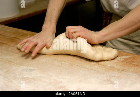 A baker's hands expertly knead and shape fresh dough on a wooden countertop in the kitchen. France Stock Photo
