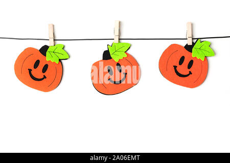 Background of halloween theme decorations. Toy pumpkins hanging on a string with wooden clothespins on white backdrop. Copy space. Flat lay style. Stock Photo