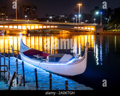 Kaohsiung, Taiwan: Italian style gondola (boat) parked at pier on Love River at night, colorful lights of bridge reflecting in water Stock Photo