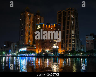 Kaohsiung, Taiwan: The Building of the Ambassador Hotel with two skyscrapers behind reflecting in Love river at night Stock Photo