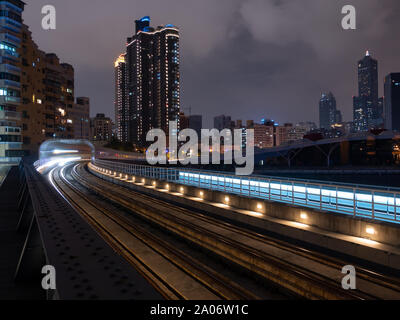 The Kaohsiung light rail track near love pier station at night, Kaohsiung City in the background. Stock Photo
