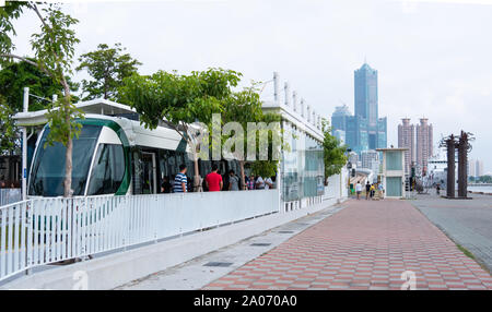 Kaohsiung, Taiwan: Kaohsiung light rail tram at station with people entering and exiting, Tuntex Sky Tower in background Stock Photo