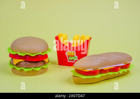 fast food. plastic hamburger, hot dog and french fries on a yellow background