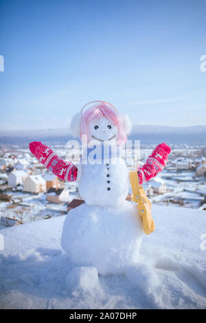 New year snowman from white snow with bag. Christmas or xmas decoration. Snowman in pink wig, mittens and scarf. Happy holiday and celebration. Winter Stock Photo