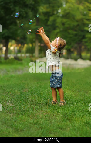 Full length portrait of a toddler girl catching soap bubbles in the summer park Stock Photo