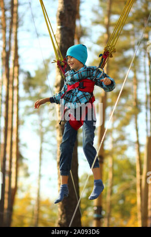 Boy jumping on a bungee trampoline and flying in the air in the autumn park outdoor Stock Photo