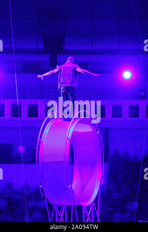Circus performer / acrobat on top of spinning wheel of death / space wheel. Dangerous job. Stock Photo