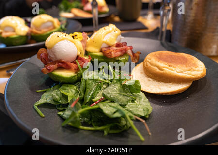 Avocado Benedict. Poached egg served on a avocado half with hollandaise sauce and bacon, bread bun and green salad on a side Stock Photo