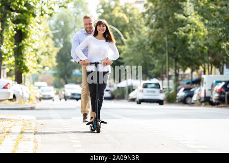 Portrait Of Happy Couple Riding On Electric Scooter Over The Street In The City Stock Photo