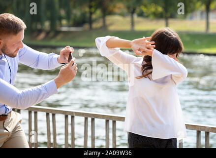 Young Woman Refusing  Man Taking Photo Of Her On Mobile Phone Stock Photo