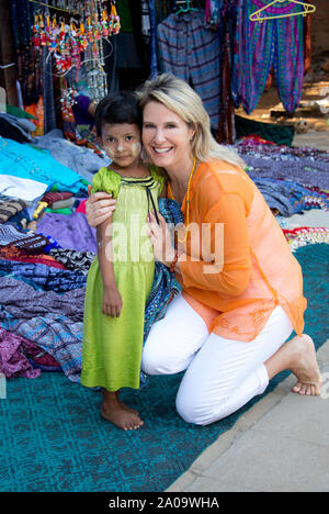A Female Caucasian Tourist (released) Posing with a Little Burmese Girl wearing Thanaka Makeup which is for Sun Protection in an Outdoor  Market in Ba Stock Photo