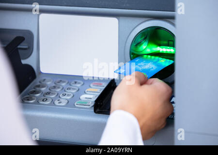 Close-up Of A Person's Hand Insert Card Into ATM Machine Slot To Withdraw Money Stock Photo