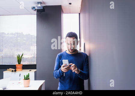 businessman standing at concrete wall looking at cell phone Stock Photo