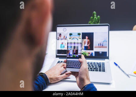 Rear view of man taking photo to laptop with smartphone Stock Photo