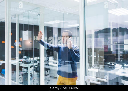 Side view of businessman talking on smart phone while standing against office wall Stock Photo