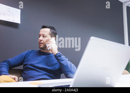 Male executive talking on mobile phone while using laptop at desk Stock Photo