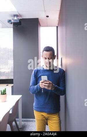 businessman standing at concrete wall looking at cell phone Stock Photo