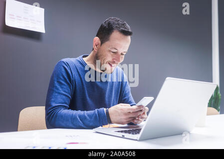 Young businessman reading his smartphone. Portrait of business man reading message with smartphone in office. Man working at his desk at office. Stock Photo