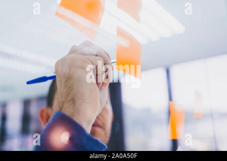 Mature businessman writing on sticky notes at glass pane in office Stock Photo