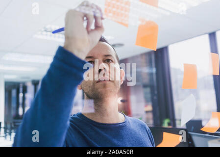 Mature businessman writing on sticky notes at glass pane in office Stock Photo
