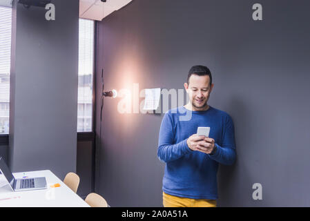 businessman standing at concrete wall looking at cell phone Stock Photo