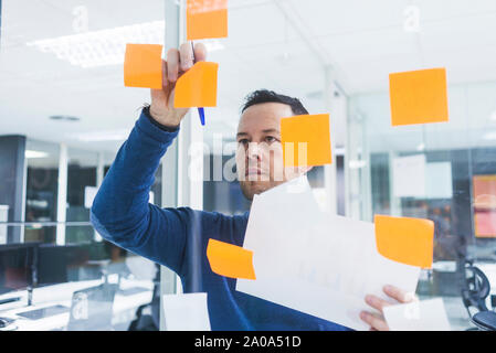 Mature businessman writing on sticky notes at glass pane in office Stock Photo