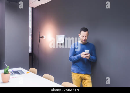 businessman standing at concrete wall looking at cell phone Stock Photo