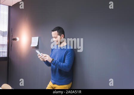 businessman standing at concrete wall looking at cell phone Stock Photo