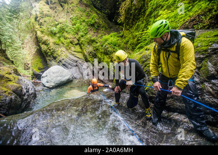 Three adventurous men work as a team to belay friend down waterfall. Stock Photo