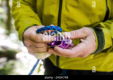 detail of man running rope through a belay device. Stock Photo