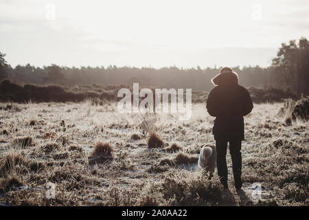 Man walking dog on frosty heathland in golden light Stock Photo