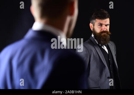 Meeting of reputable businessmen, black background. Man with beard on suspicious face, and shoulders of partner, defocused. Business meeting concept. Stock Photo