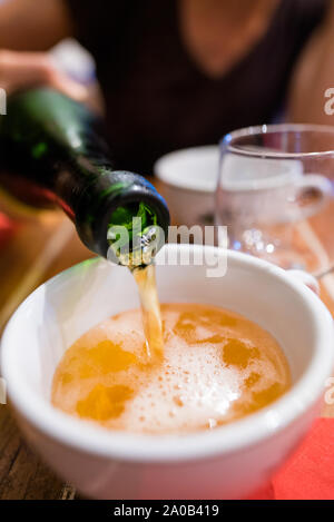 Verical selective focus view of a slim woman pouring fresh organic Norman apple cider into the traditional ceramic cups at a dinner party Stock Photo