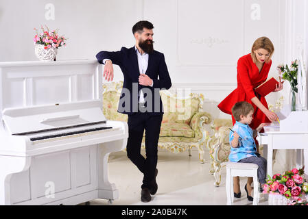 Home schooling concept. Kid growthing in welfare. Parents enjoying parenthood, carefree, happy. Father stands near piano, watching while mother teache Stock Photo