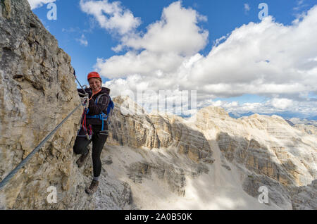 Horizontal view of an attractive blonde female climber on a steep Via Ferrata in the Italian Dolomites with a great view behind Stock Photo