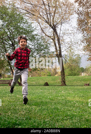 Smiling young boy running through the grassy field, having fun, concepts of innocence and cheerfulness, positive human emotions. Stock Photo