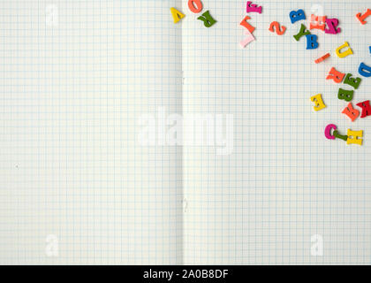 open notebook with white sheets in a box and small multi-colored wooden letters, back to school, copy space Stock Photo