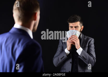 Man with beard on calm face sniffing money, smell of profit. Meeting of reputable businessmen, black background. Business payment concept. Businessmen Stock Photo