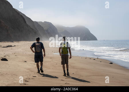 Wildcat Beach, California - August 30, 2019: Two hikers walk along sandy beach between sheer cliffs and Pacific Ocean on coastal route to Alamere Fall Stock Photo